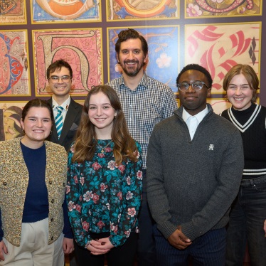 Group of six individuals smiling in front of a colorful, patterned wall with artistic designs.