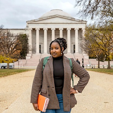 Person standing in front of the National Gallery of Art in Washington D.C., holding a book and wearing a plaid blazer.
